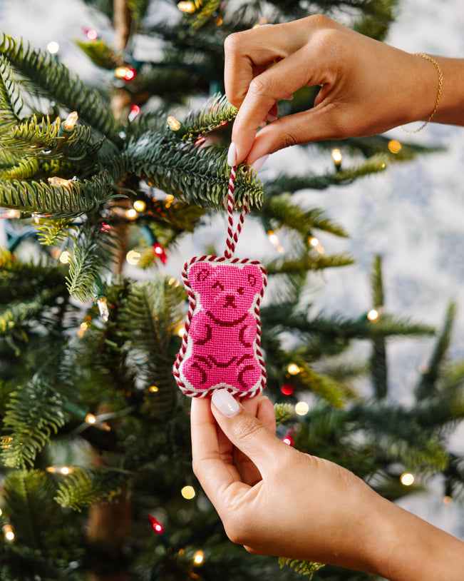 Pink teddy bear ornament being hung on a Christmas tree