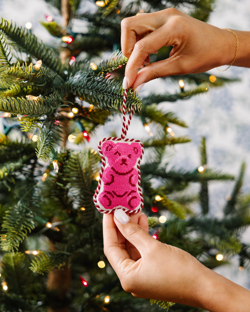 Pink teddy bear ornament being hung on a Christmas tree