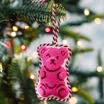 Pink teddy bear ornament hanging on a Christmas tree with blurred lights in the background