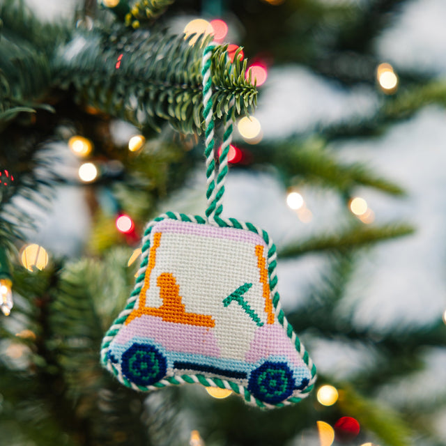 Decorative ornament shaped like a bell hanging on a Christmas tree with blurred lights in the background.