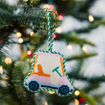 Decorative ornament shaped like a bell hanging on a Christmas tree with blurred lights in the background.