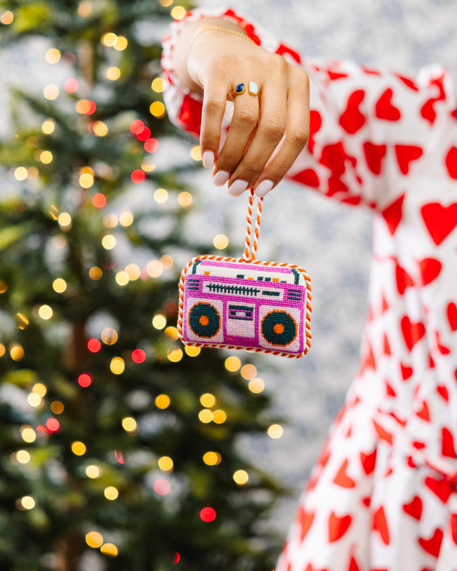 Hand holding a pink boombox ornament in front of a decorated Christmas tree.
