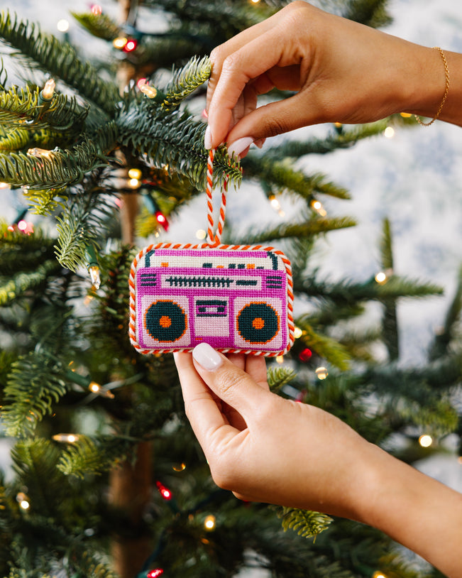 Hand holding a colorful boombox ornament against a Christmas tree background