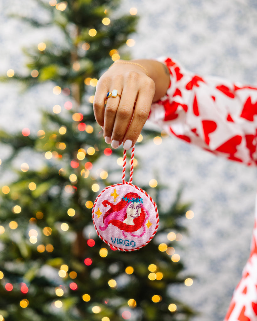 Person holding a decorative ornament with a Christmas tree in the background