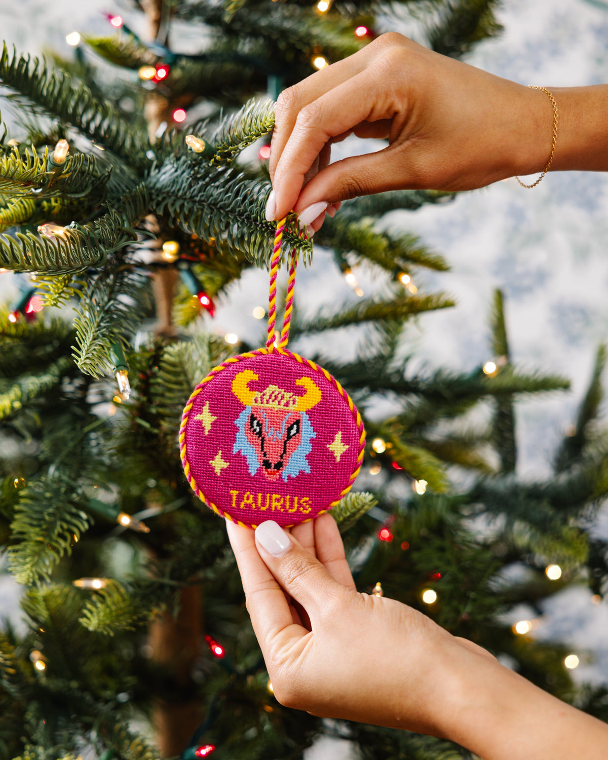 Hand holding a Taurus zodiac ornament on a decorated Christmas tree.