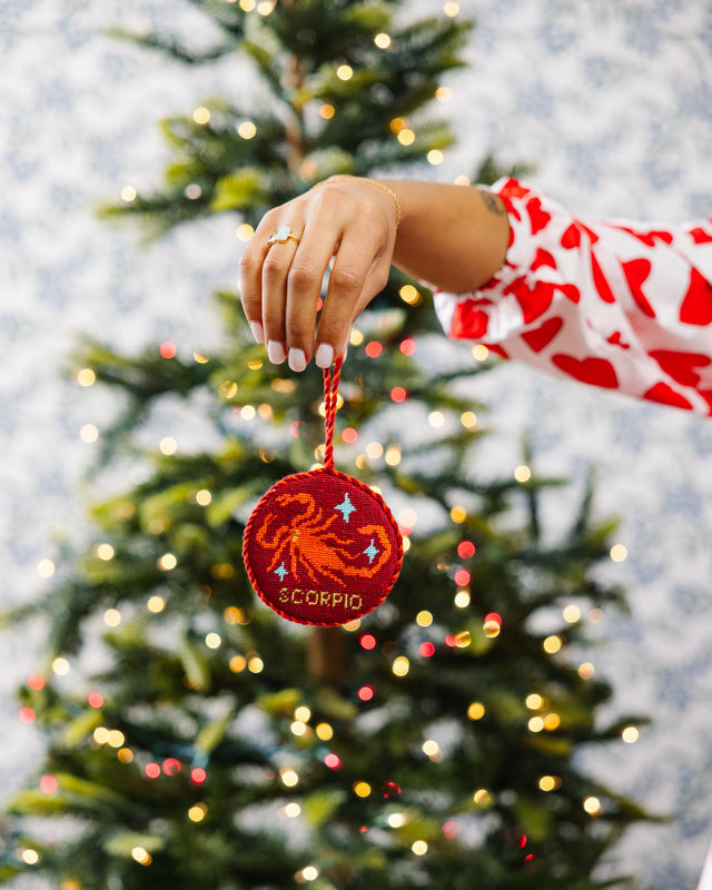 Hand placing a Scorpio zodiac ornament on a decorated Christmas tree.