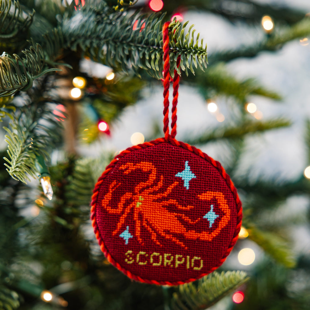 Red 'Scorpio' zodiac ornament on a Christmas tree with blurred lights in the background