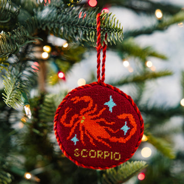 Red 'Scorpio' zodiac ornament on a Christmas tree with blurred lights in the background
