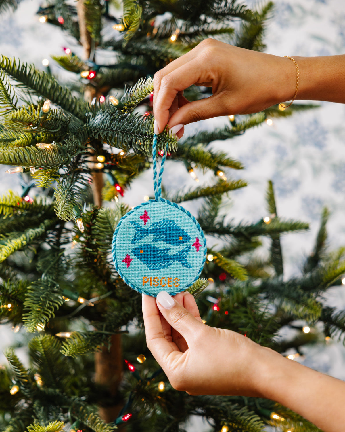 Hand holding a blue ornament with a whale design against a Christmas tree background