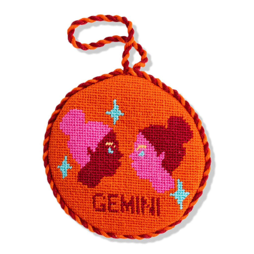 Round orange ornament with embroidered designs and 'Gemini' text on a white background