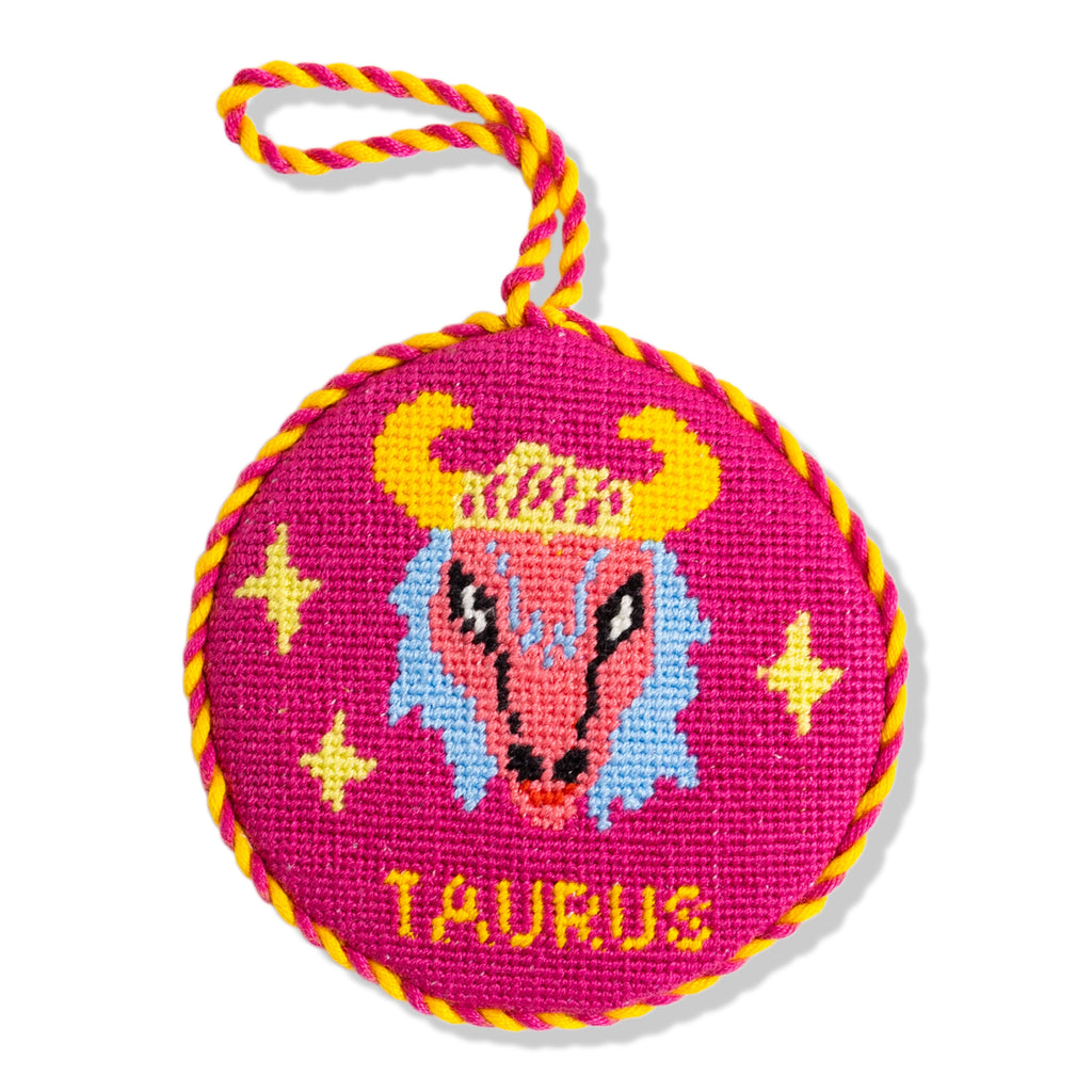 Circular pink needlepoint with Taurus design and yellow rope handle on a white background