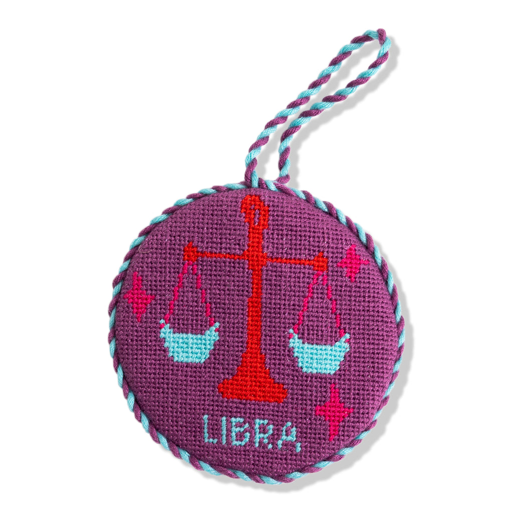 Round purple needlepoint ornament with Libra design on a white background