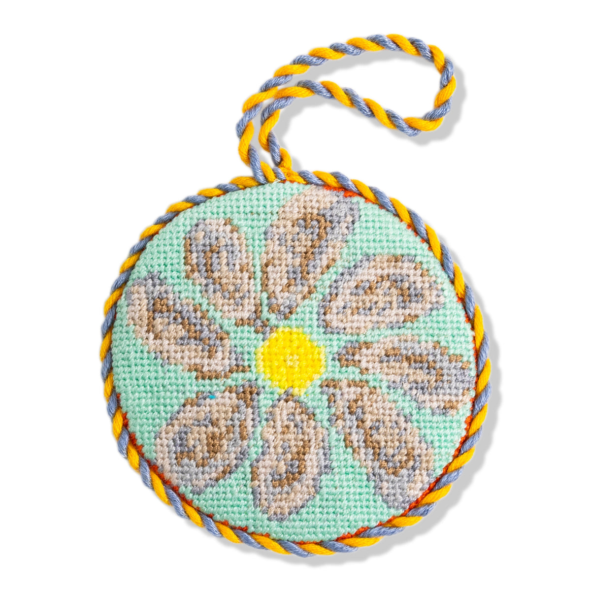 Round needlepoint ornament with floral design and colorful rope on a white background