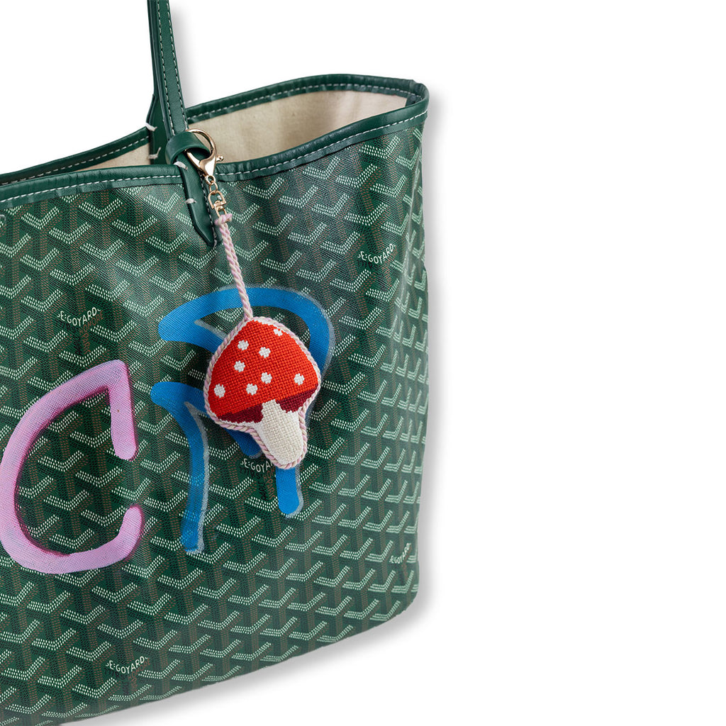Green patterned handbag with a decorative charm featuring a mushroom and letter 'C'.