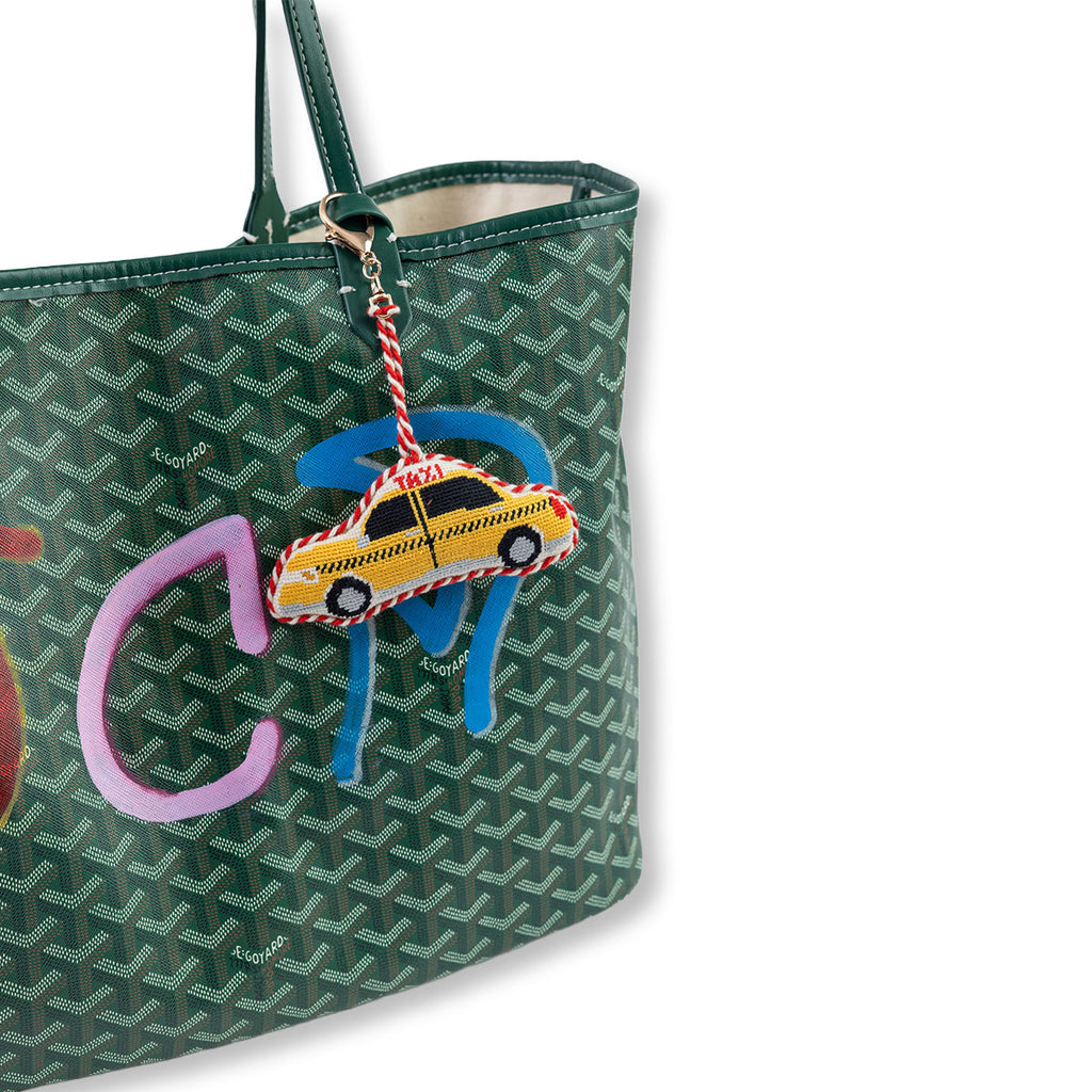 Green patterned handbag with a colorful charm featuring a taxi and pink elephant on a white background