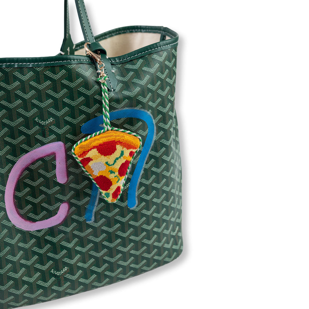 Green patterned handbag with a colorful pizza charm and pink letter 'C' on a white background