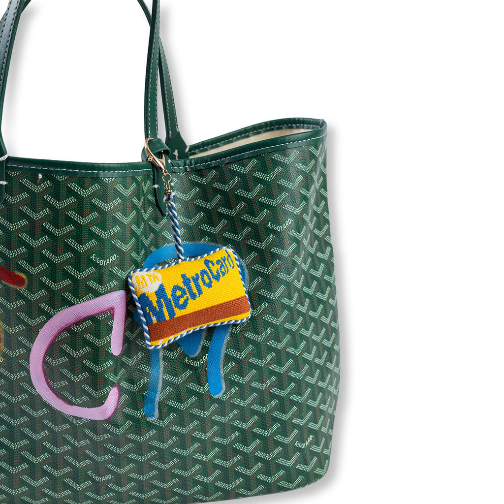 Green patterned handbag with a colorful 'New York City Subway' keychain on a white background