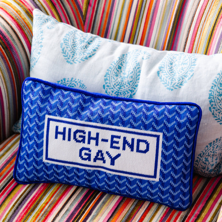 Decorative pillow with 'HIGH-END GAY' text on a colorful striped sofa.