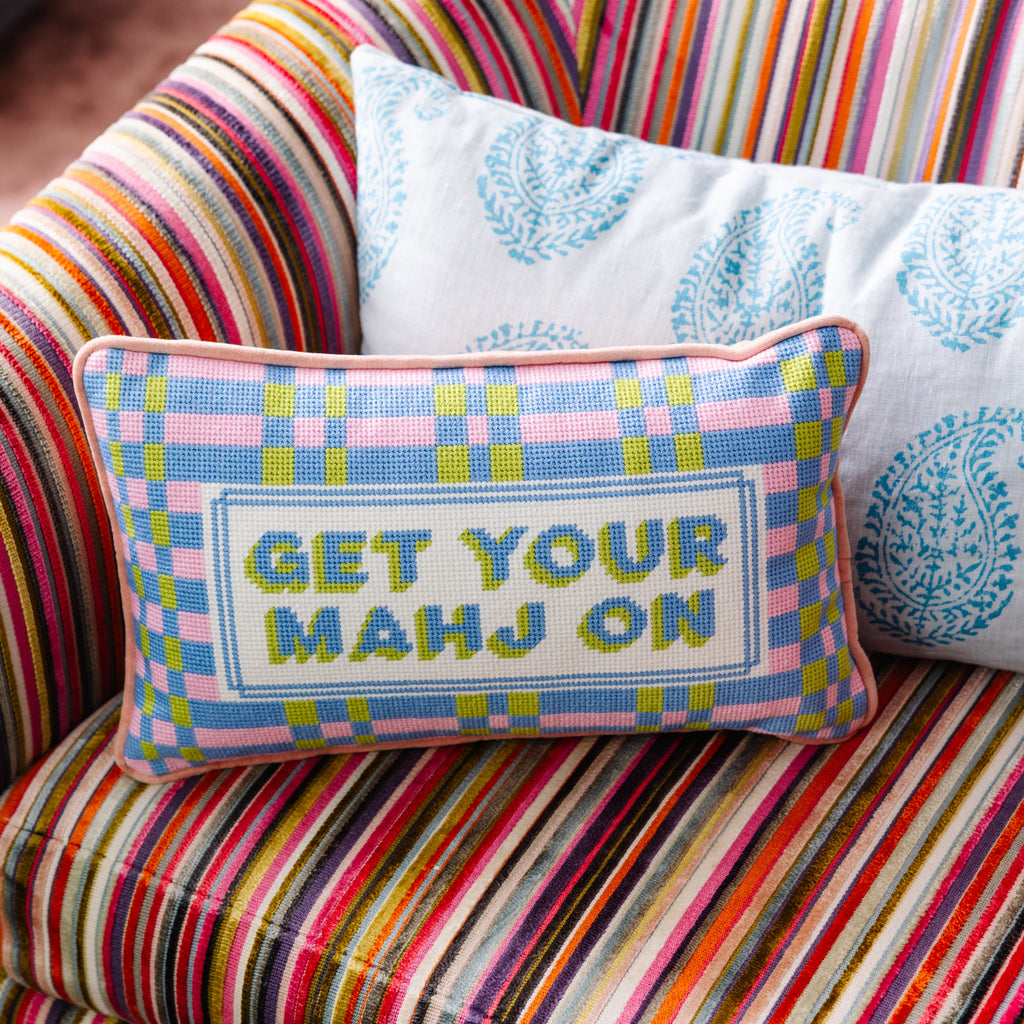 Decorative pillow with 'GET YOUR MAHJ ON' text on a colorful striped couch.