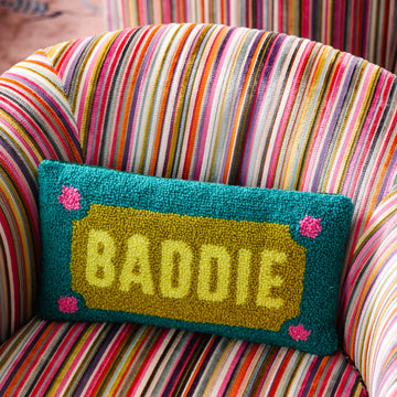 Colorful striped chair with a pillow that says 'BADDIE' on a multicolored background