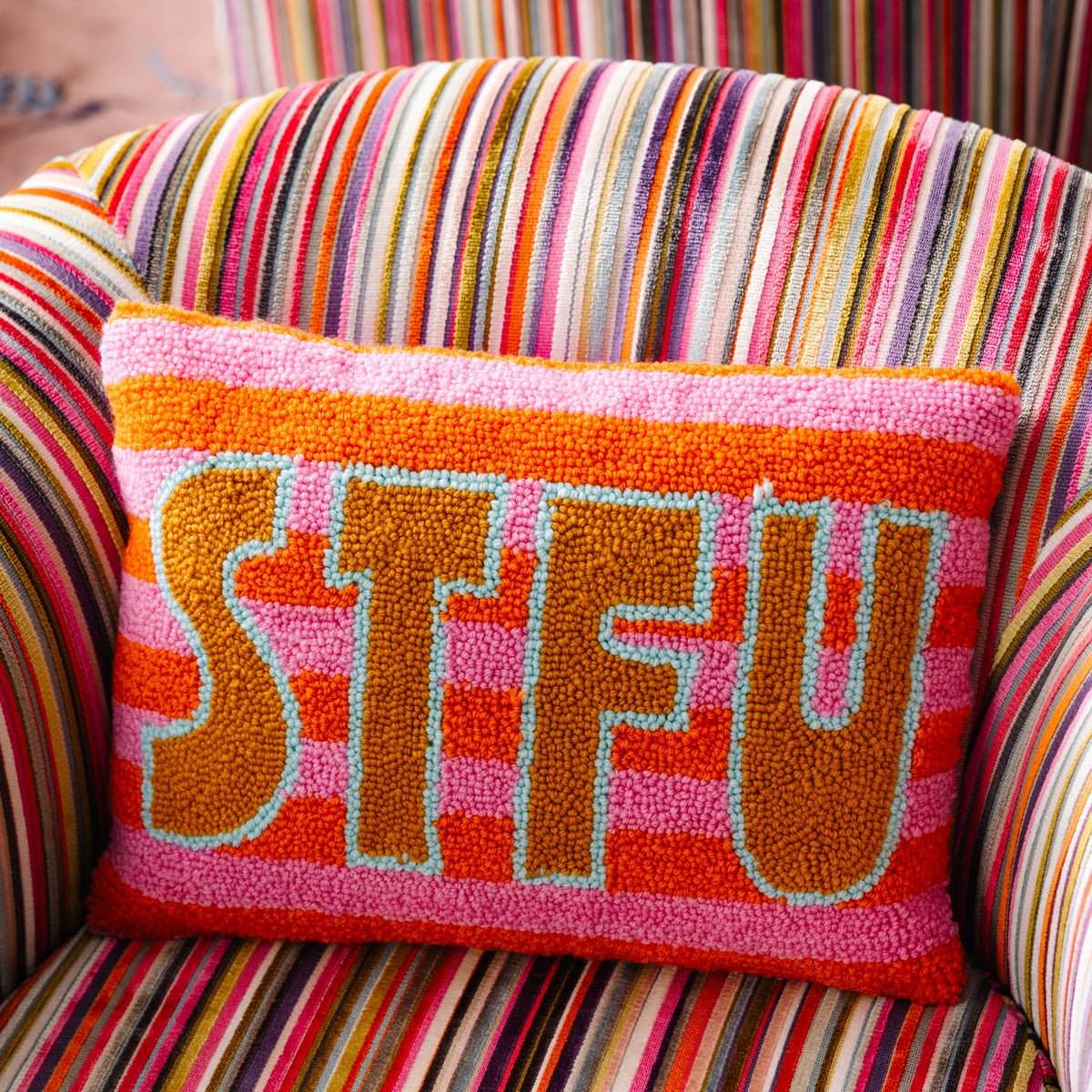 Colorful pillow with 'STFU' text on a striped chair