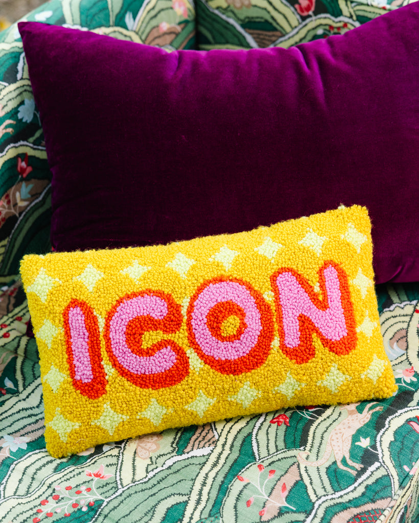 Yellow pillow with 'ICON' embroidery on a patterned fabric background
