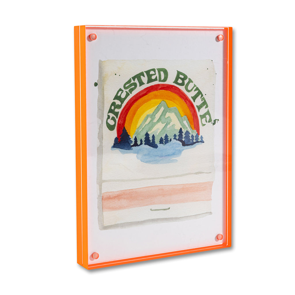 Crested Butte Matchbook - Furbish Studio, A matchbook watercolor print illustrating the Crested Butte Ski Resort's surroundings through a watercolor paint and it is below the dark green painted "Crested Butte" enclosed in a 5" x 7" orange magnetic acrylic floating frame facing a side view