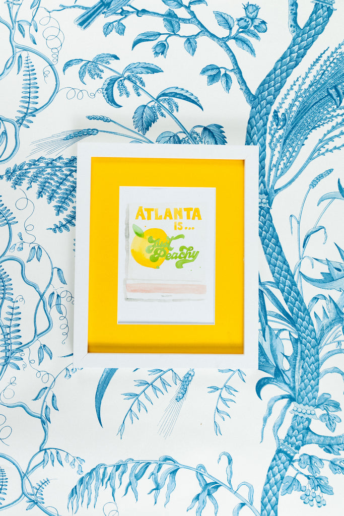 Atlanta Matchbook - Furbish Studio, Atlanta matchbook watercolor print with a yellow peach fruit paint under the saying "Atlanta is... Just Peachy" in a 5x7 white frame with a wallpaper background