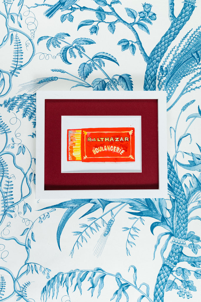 Balthazar Matchbook - Furbish Studio, Balthazar Boulangerie matchbook watercolor print that features a red orange background design taken from the iconic French bakery, Balthazar Boulangerie in a 5x7 white frame with a wallpaper background