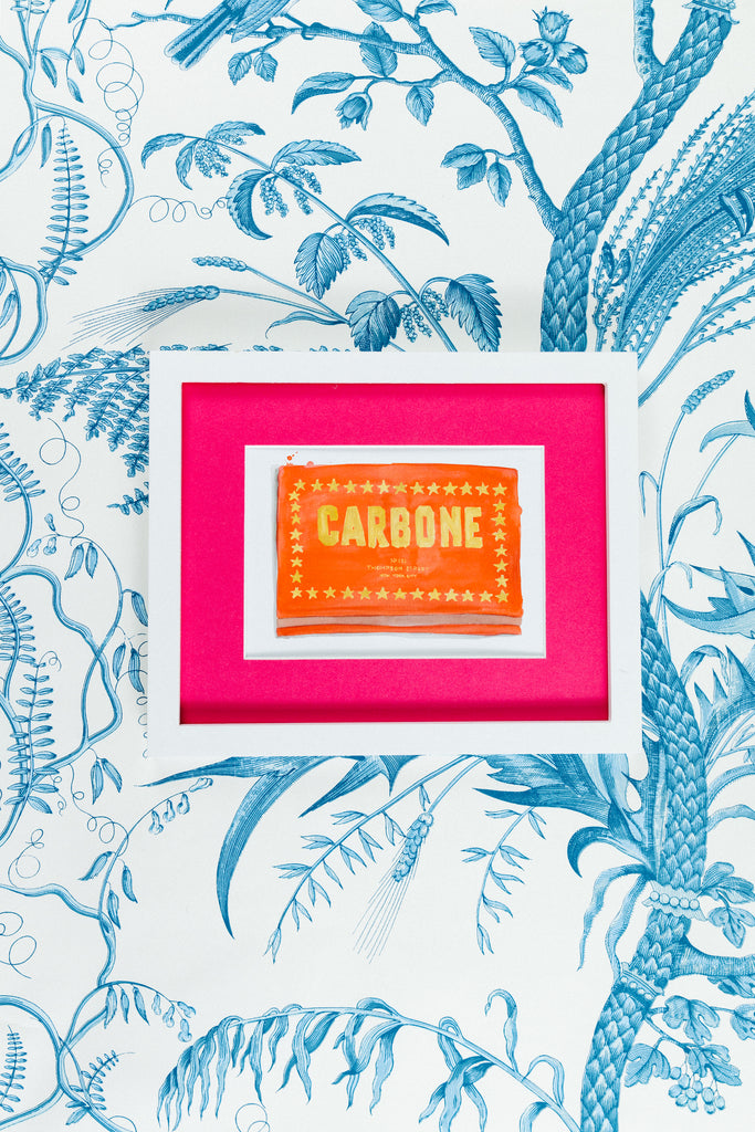 Carbone Matchbook - Furbish Studio, A matchbook watercolor print with gold painted "Carbone" surrounded by gold stars in a rectangle formation with an orange background color in a 5x7 white frame with a wallpaper background