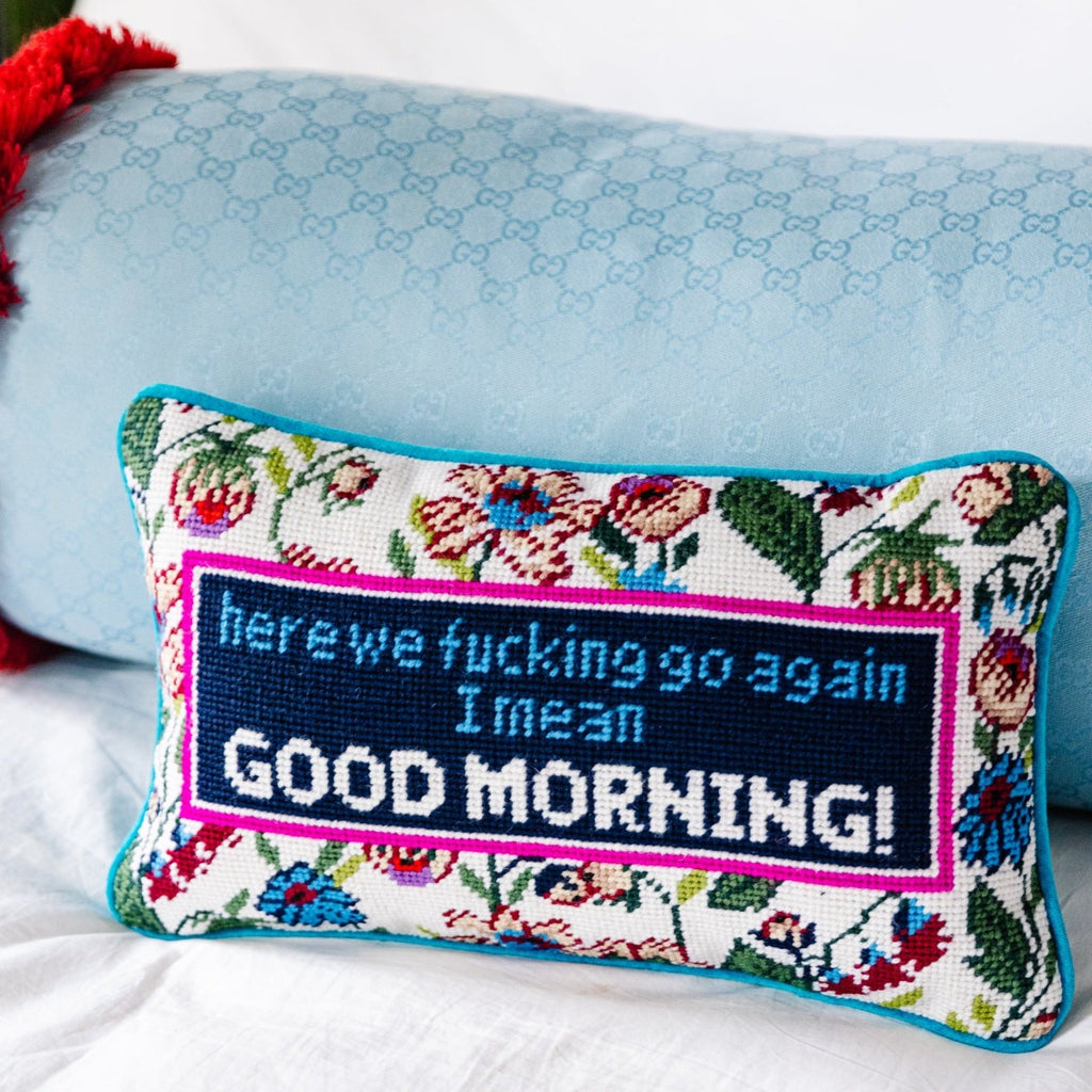 hand embroidered in wool and backed in luxe blue green velvet chic needlepoint pillow with "here we fucking go again, I mean Good morning!" cheeky saying in front with a light blue bolster pillow at the back of it