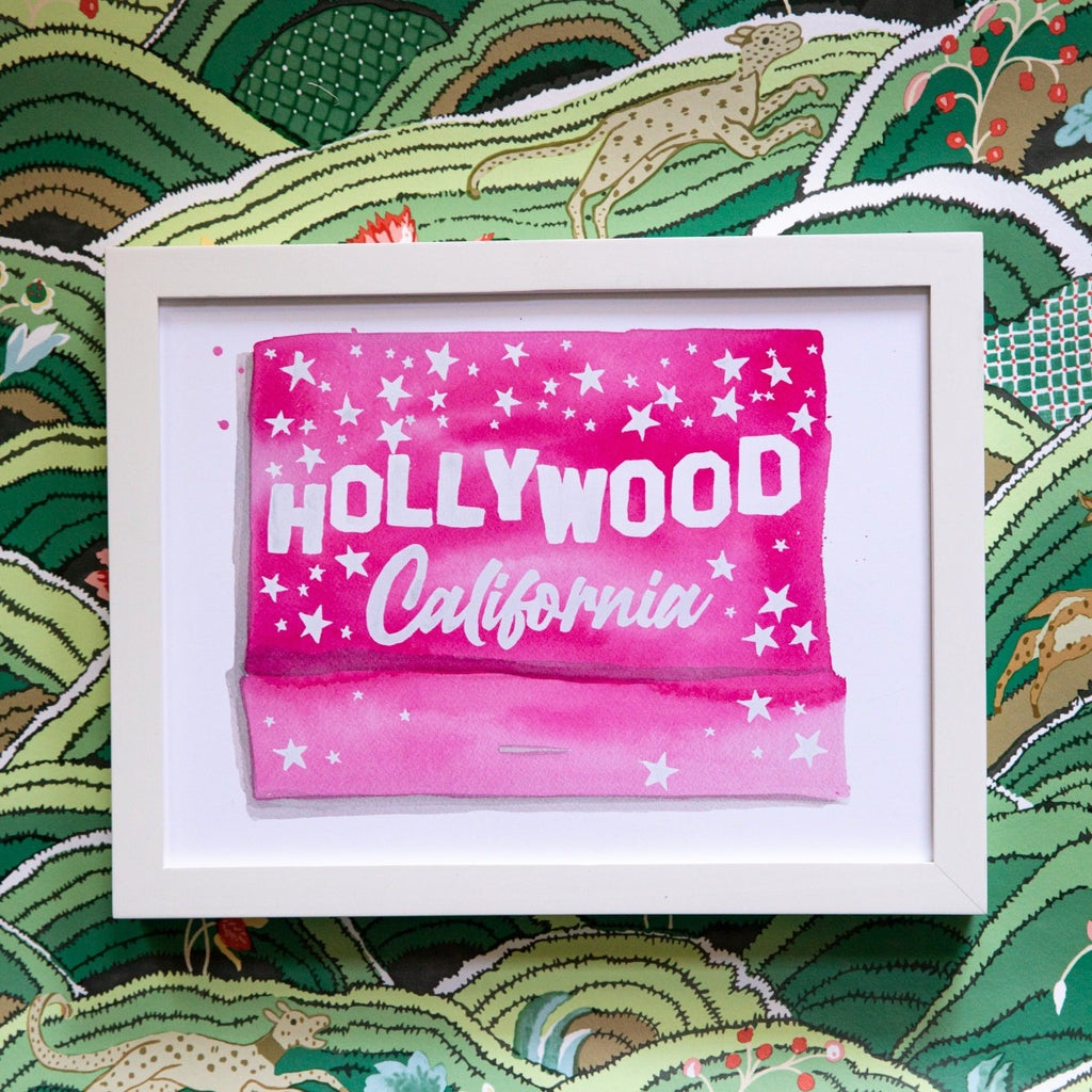 Hollywood Matchbook - Furbish Studio, A Hollywood matchbook watercolor print painted in pink with the title Hollywood California painted in white surrounded by white stars in a white frame attached to the wall
