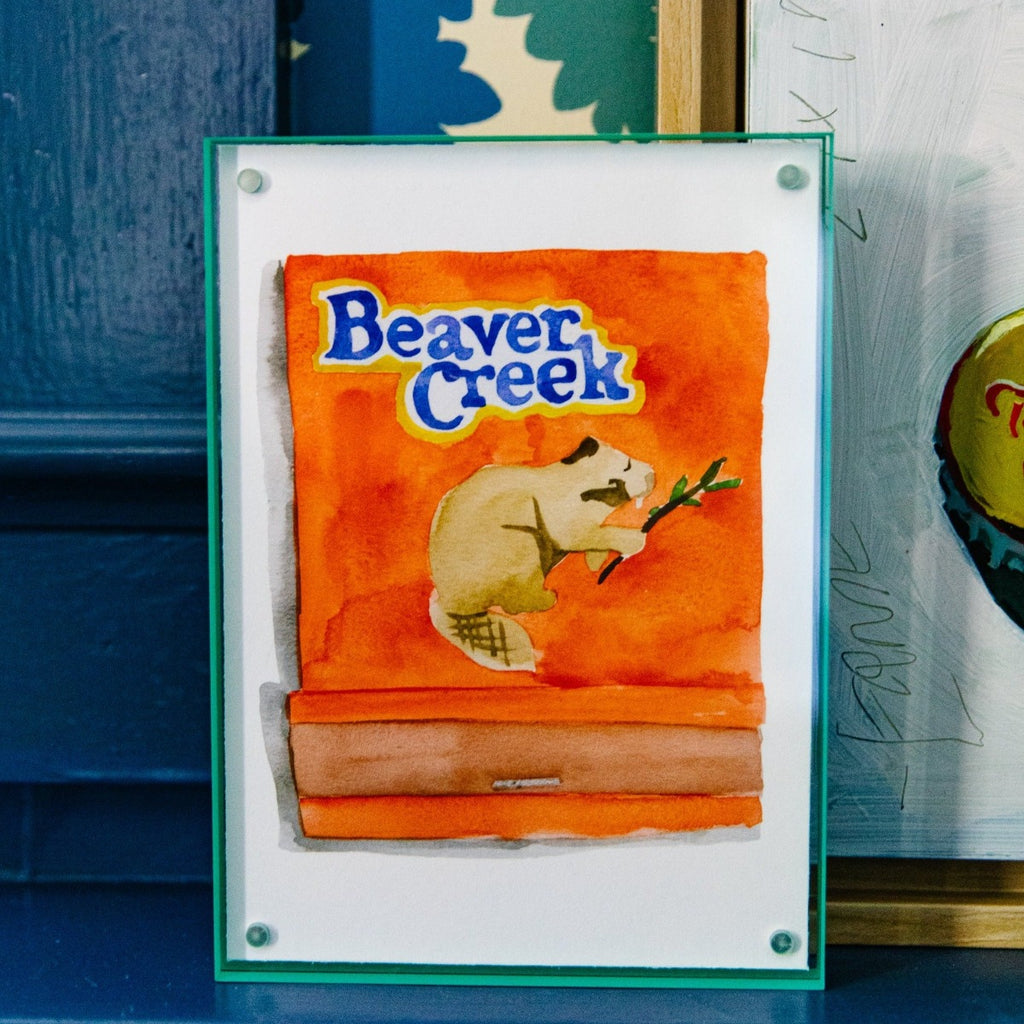 Beaver Creek Matchbook - Furbish Studio, A Beaver Creek matchbook watercolor print featuring a beaver holding a branch with an orange background color paint enclosed in a 5" x 7" mint-green magnetic acrylic floating frame