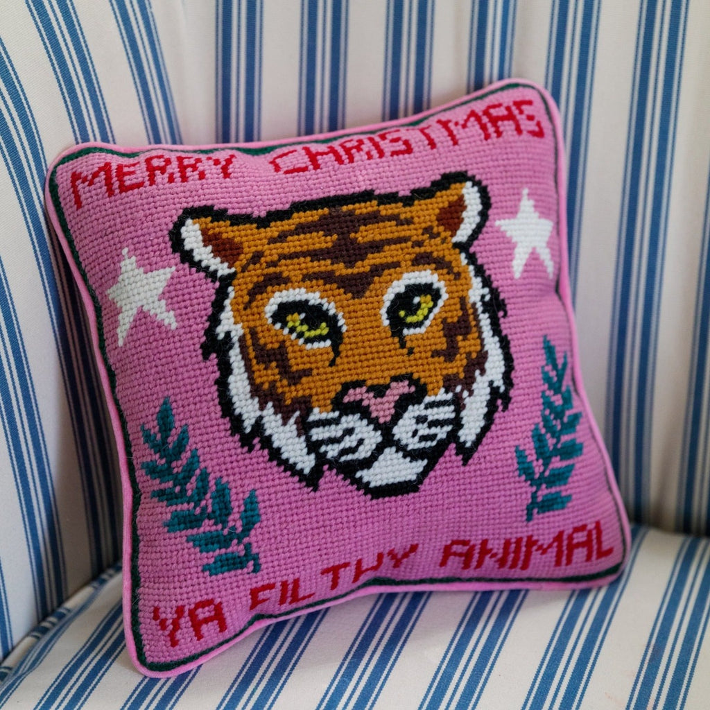 hand embroidered in wool and backed in luxe pink velvet chic needlepoint pillow with "Merry Christmas Ya Filthy Animal" cheeky saying in front  sitting on a couch